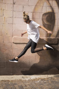 a girl jumps high off the stone street in her athletic shoes