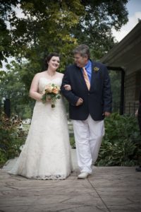 father lovingly looks at his daughter while walking her down the aisle at an outdoor ceremony